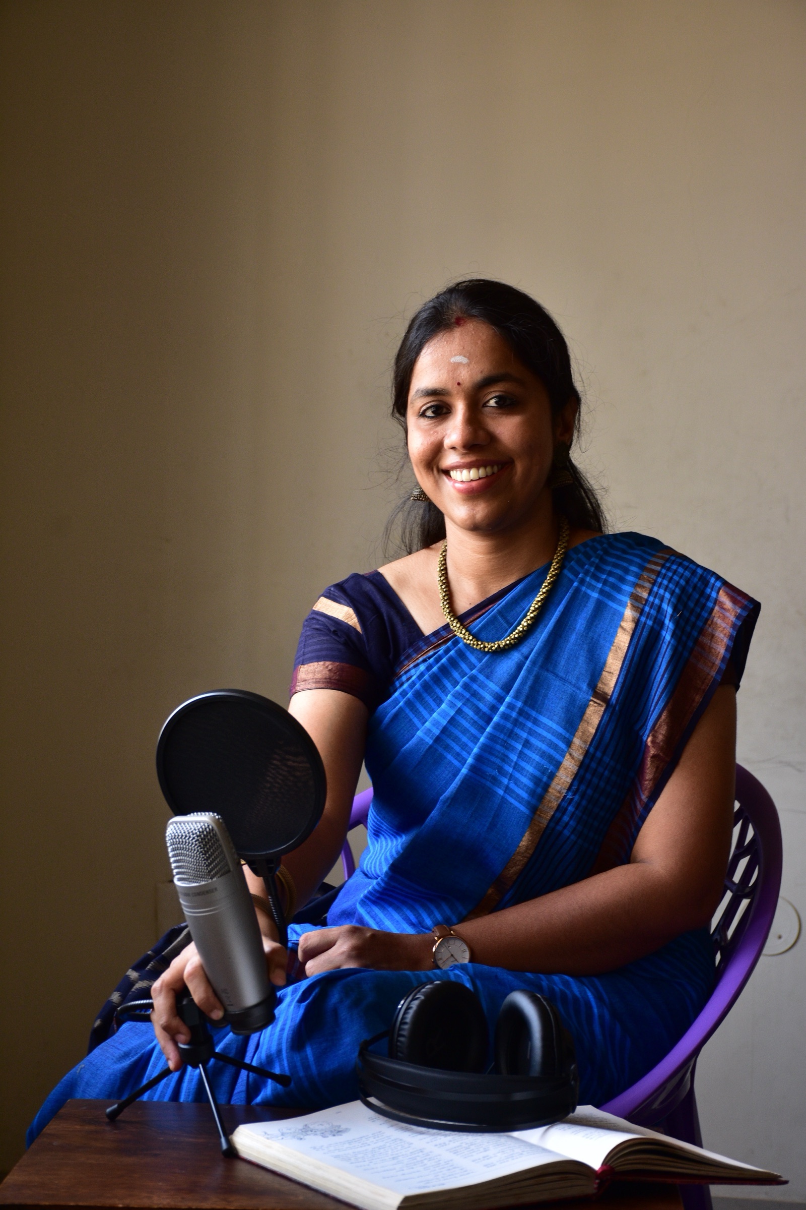 Deepika Arun at her home recording setup — microphone, headphones, and an open book